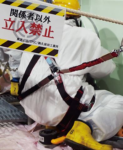 防護服を着用した作業員が安全帯を使用し作業区域で作業する様子