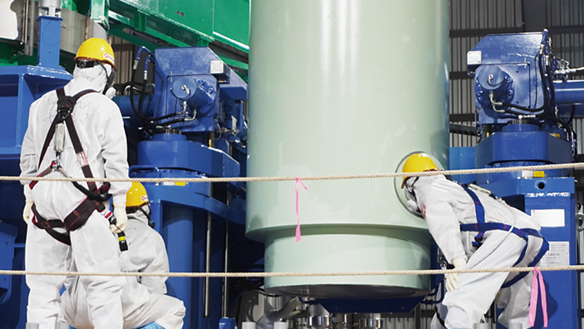 複数の作業員が大型円筒機器周辺で位置確認を行う作業状況